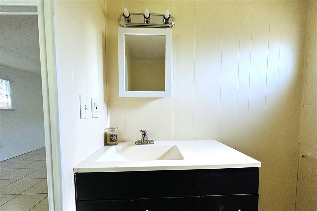 A bathroom vanity features a white countertop, a black cabinet, and a wall-mounted mirror — 1845 DIXIE LANE, HOLIDAY, FL