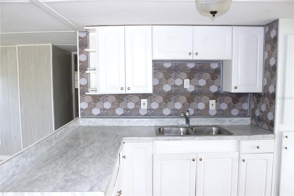 A kitchen features white cabinets, a grey laminate countertop, and a patterned hexagonal tile backsplash — 1845 DIXIE LANE, HOLIDAY, FL