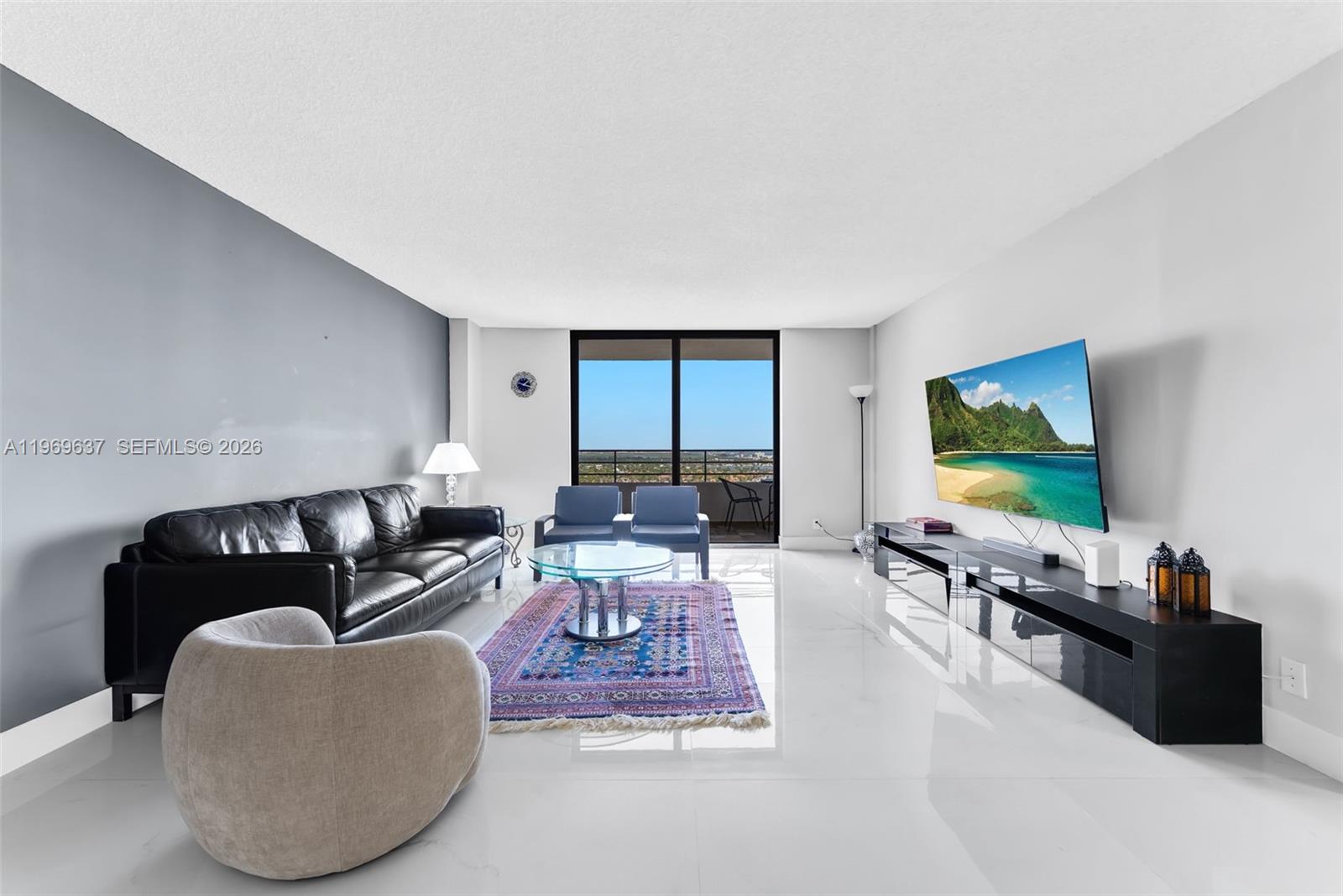 A living room features a black leather sofa, a glass coffee table, and a wall-mounted television — 2500 PARKVIEW DR # 2407, Hallandale Beach FL 33009, HALLANDALE BEACH, FL