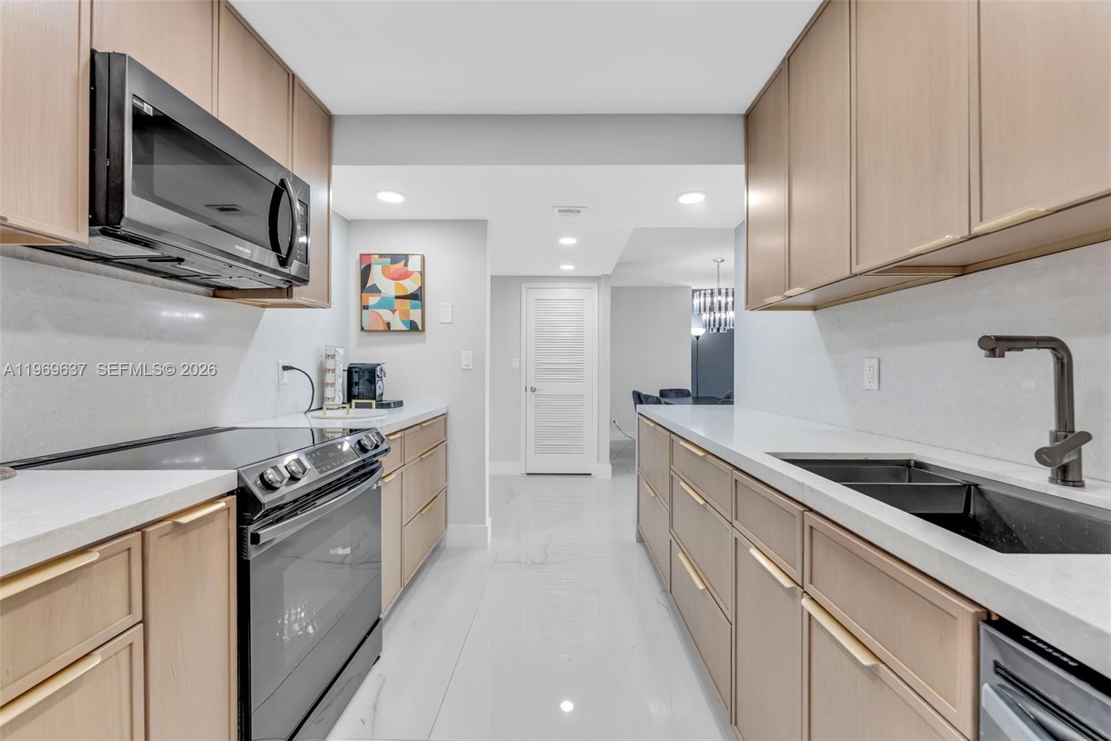 A galley kitchen features light wood cabinets, white countertops, and stainless steel appliances — 2500 PARKVIEW DR # 2407, Hallandale Beach FL 33009, HALLANDALE BEACH, FL