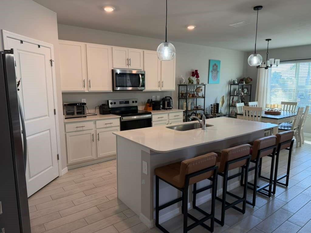A kitchen with white cabinets, a large quartz island, and bar seating on wood floors — 25275 ALCAZAR DRIVE, PUNTA GORDA, FL