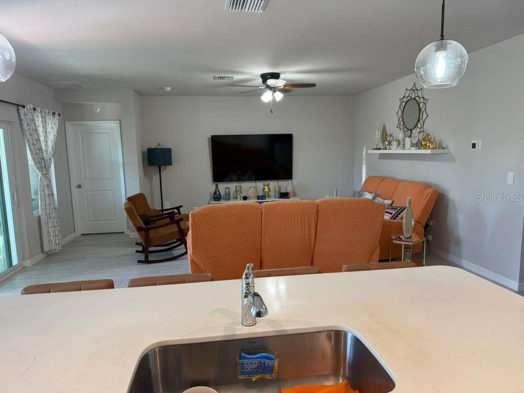 A kitchen island overlooks a living room with an orange sofa and a wall-mounted television — 25275 ALCAZAR DRIVE, PUNTA GORDA, FL