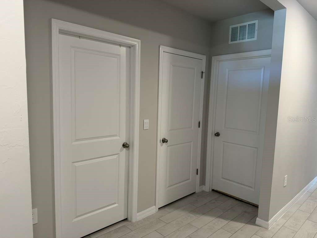 A hallway with three white paneled doors, light gray walls, and light-colored tile flooring — 25275 ALCAZAR DRIVE, PUNTA GORDA, FL