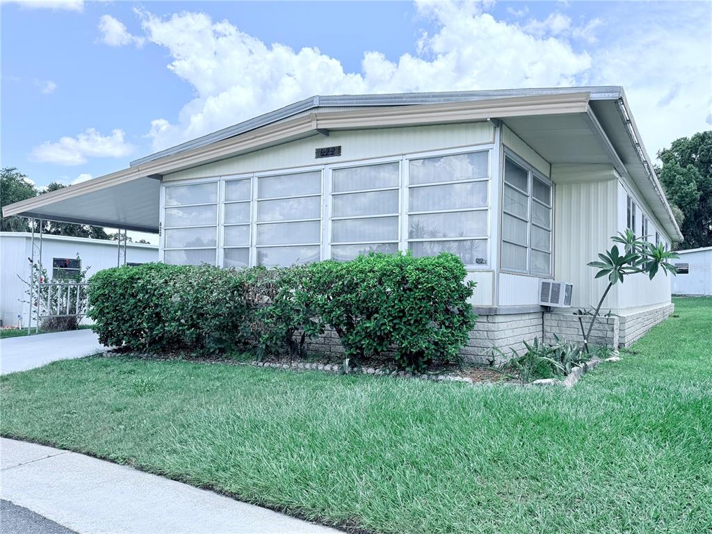 A single-story manufactured home features a large screened-in porch, a carport, and manicured landscaping — 622 ELIZABETH LANE, LAKELAND, FL