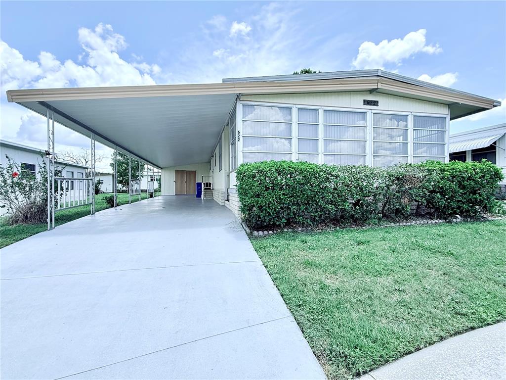 A mobile home features a large carport, a screened-in porch, and a manicured hedge — 622 ELIZABETH LANE, LAKELAND, FL