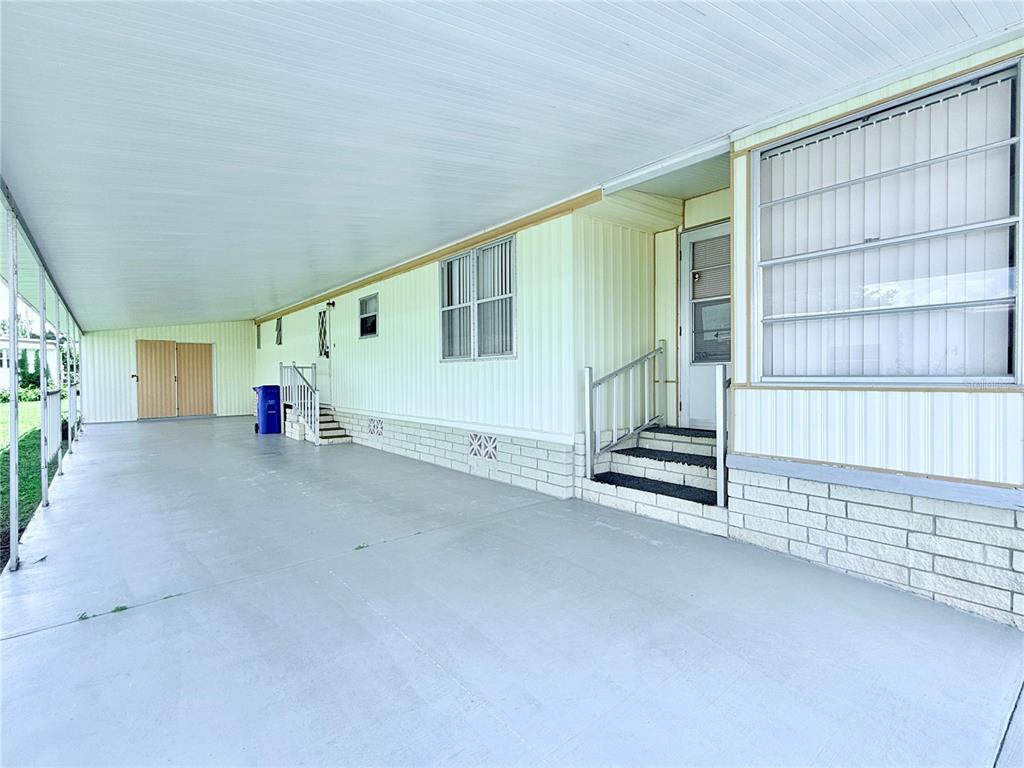A covered carport area features a concrete floor, light-colored siding, and steps leading to a door — 622 ELIZABETH LANE, LAKELAND, FL