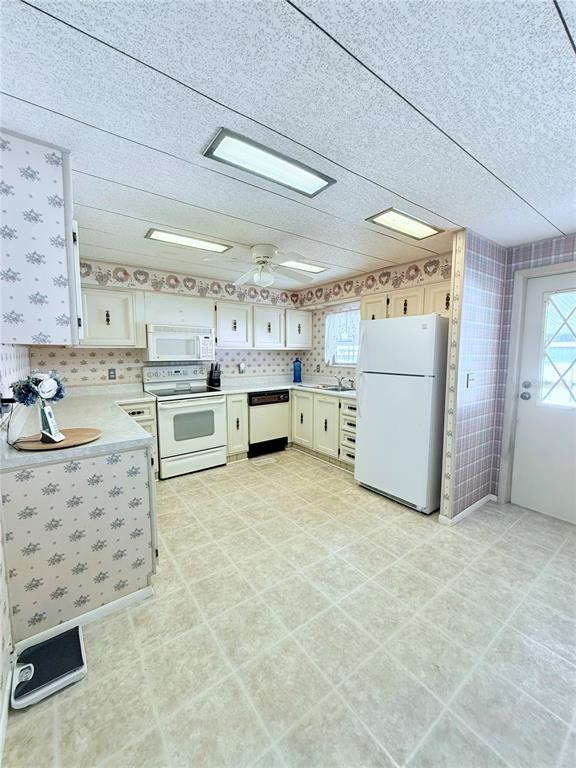 A kitchen features white cabinets, a white refrigerator, a stove, and patterned wallpaper — 622 ELIZABETH LANE, LAKELAND, FL