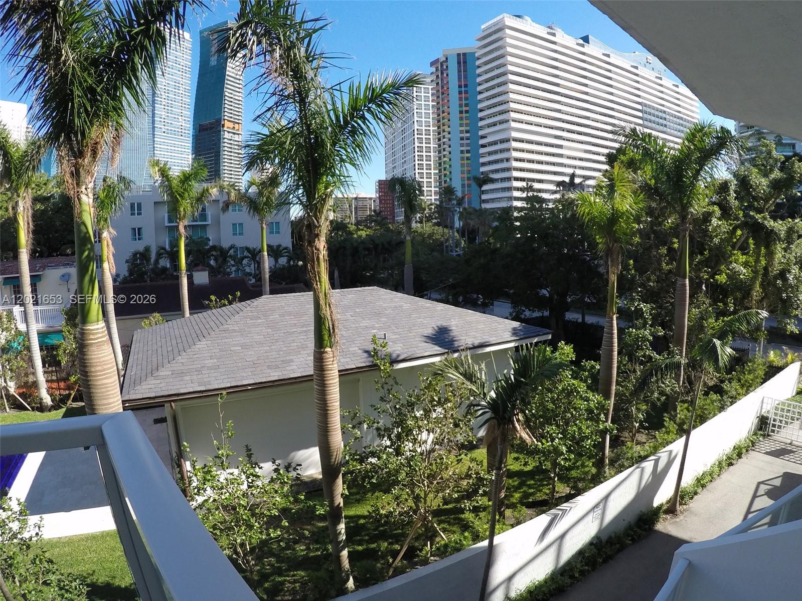 An elevated view shows palm trees, a small building with a gray roof, and skyscrapers — 1650 Brickell Ave # 110, Miami FL 33129, MIAMI, FL