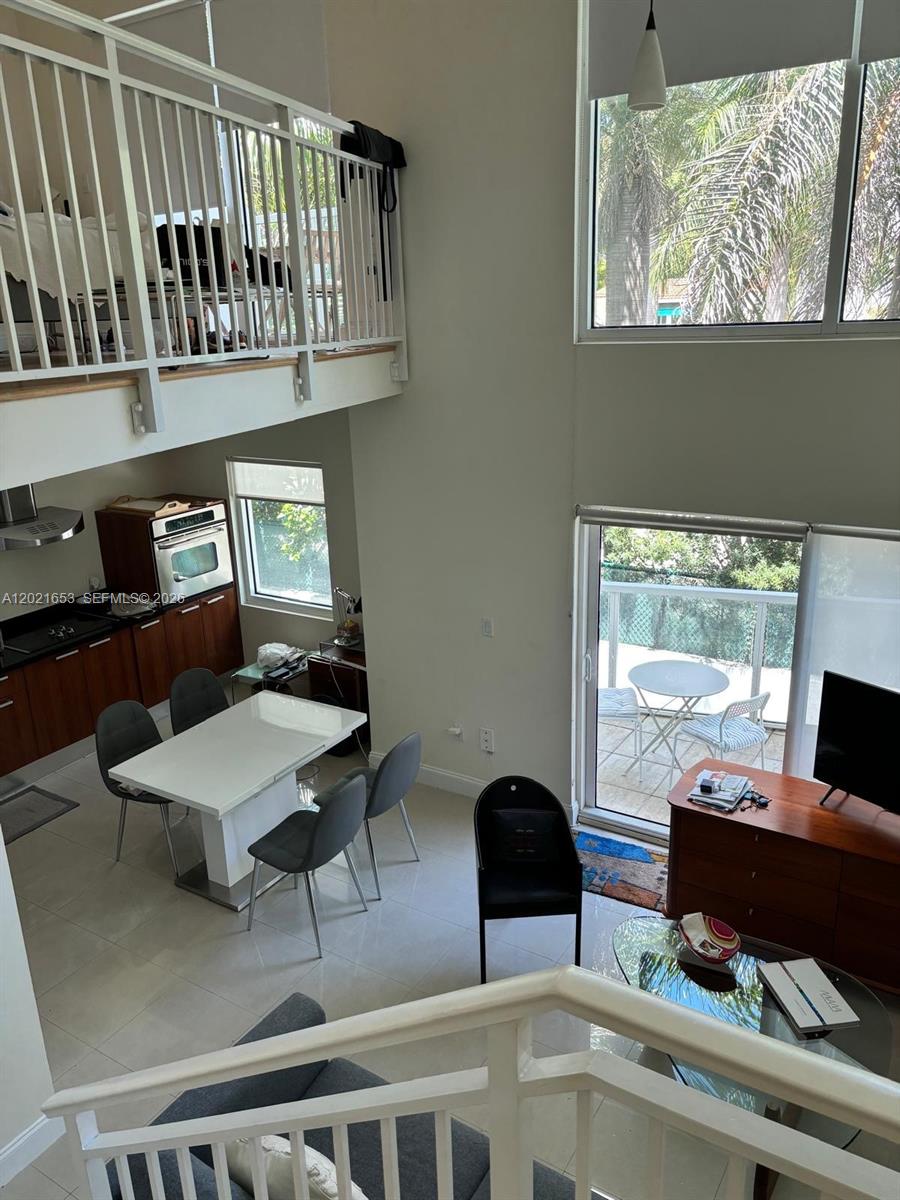 A high-ceilinged living and dining area features a lofted bedroom, tile floors, and patio access — 1650 Brickell Ave # 110, Miami FL 33129, MIAMI, FL