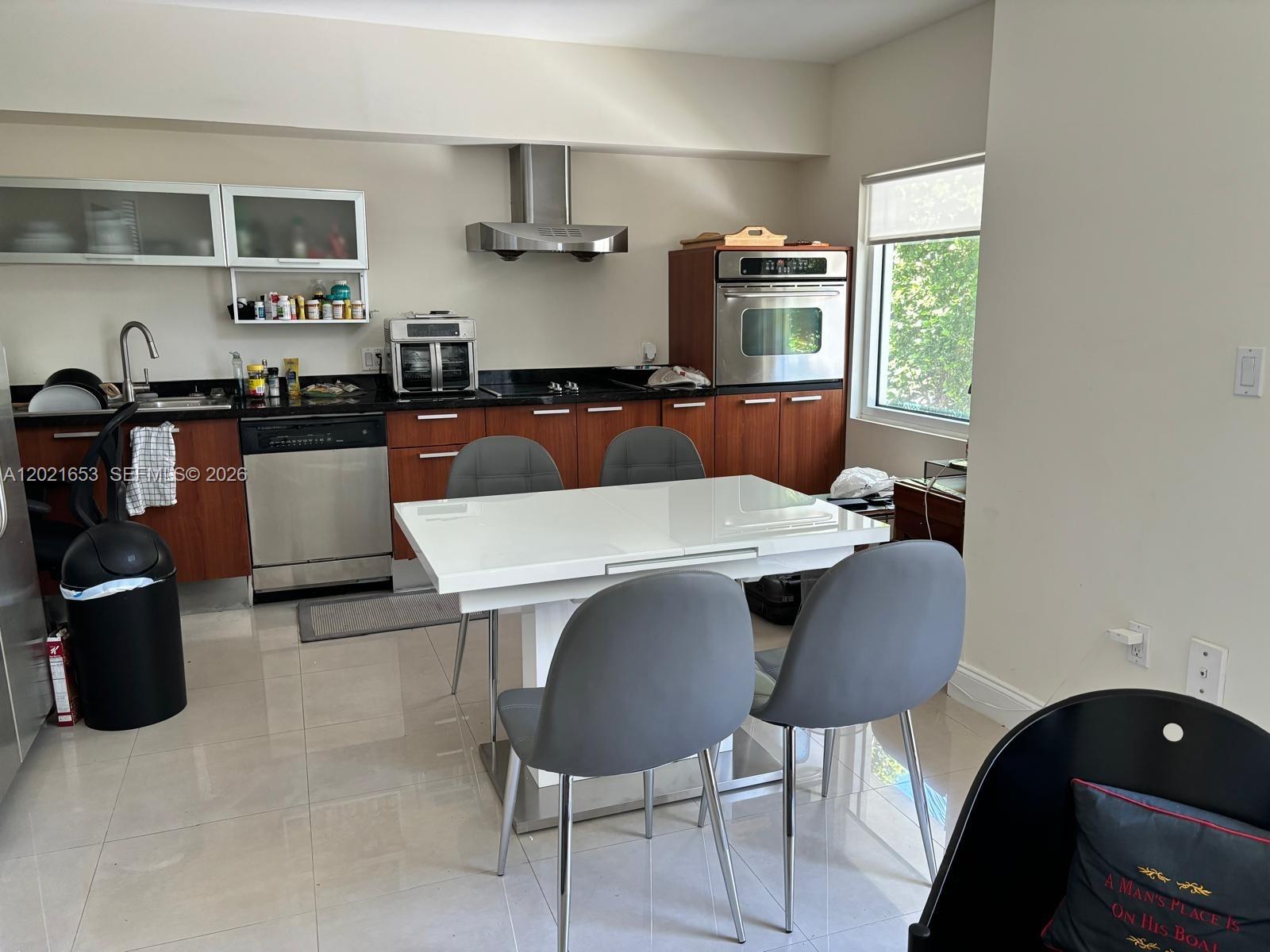 A kitchen with wood cabinets, stainless steel appliances, and a white dining table with chairs — 1650 Brickell Ave # 110, Miami FL 33129, MIAMI, FL