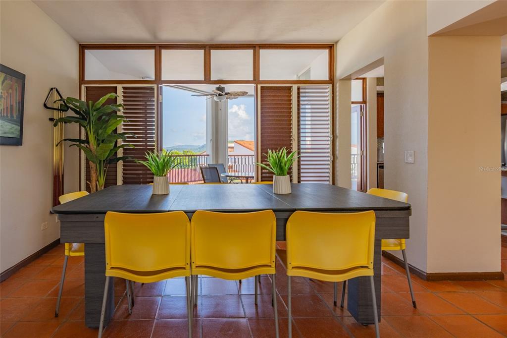 A dining room features a dark table with yellow chairs and a view of hills — 6000 RIO MAR BLVD VILLA LAS BRISAS UNIT 4A, RIO GRANDE, PR