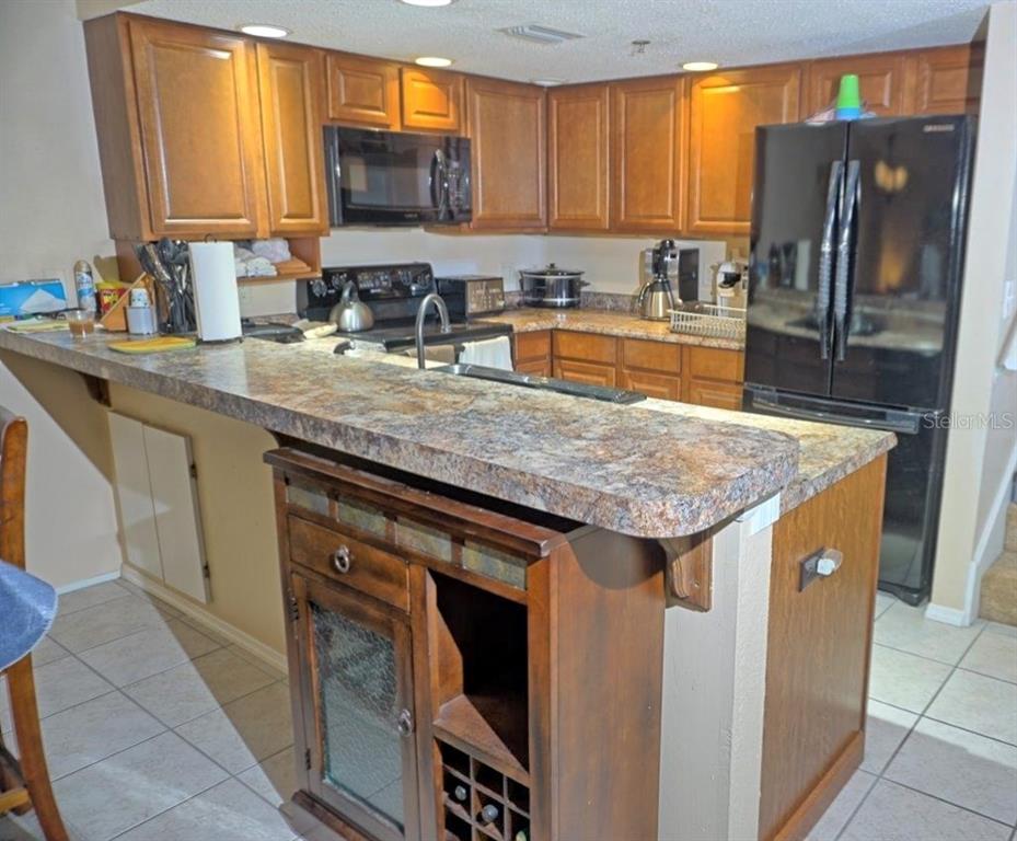A kitchen features wood cabinets, laminate countertops, a breakfast bar, and black appliances — 2051 VISTA DEL SOL CIRCLE UNIT 202, LUTZ, FL