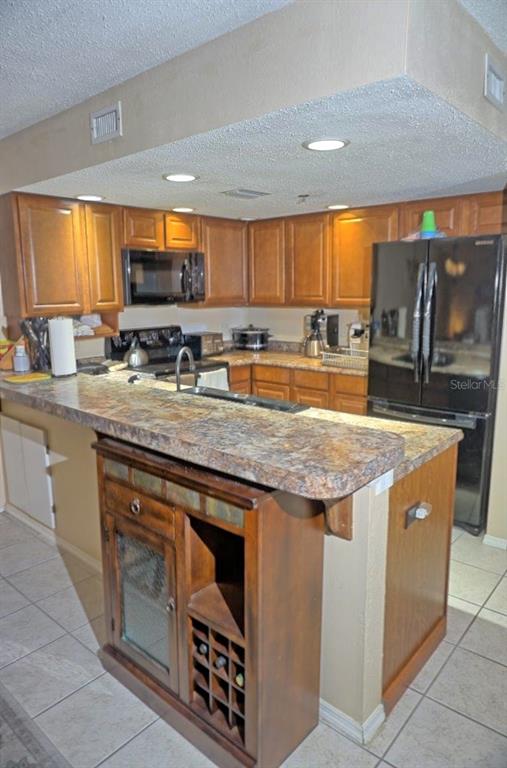 A kitchen features wood cabinets, a stone-look countertop, a breakfast bar, and a wine rack — 2051 VISTA DEL SOL CIRCLE UNIT 202, LUTZ, FL