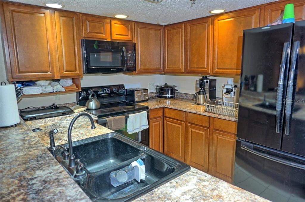 A kitchen features wood cabinets, granite countertops, a black sink, and black appliances — 2051 VISTA DEL SOL CIRCLE UNIT 202, LUTZ, FL
