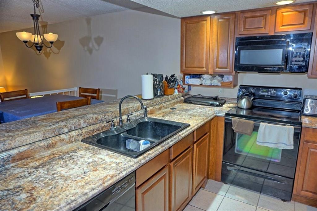 A kitchen with wood cabinets, granite countertops, and black appliances overlooks a dining area — 2051 VISTA DEL SOL CIRCLE UNIT 202, LUTZ, FL