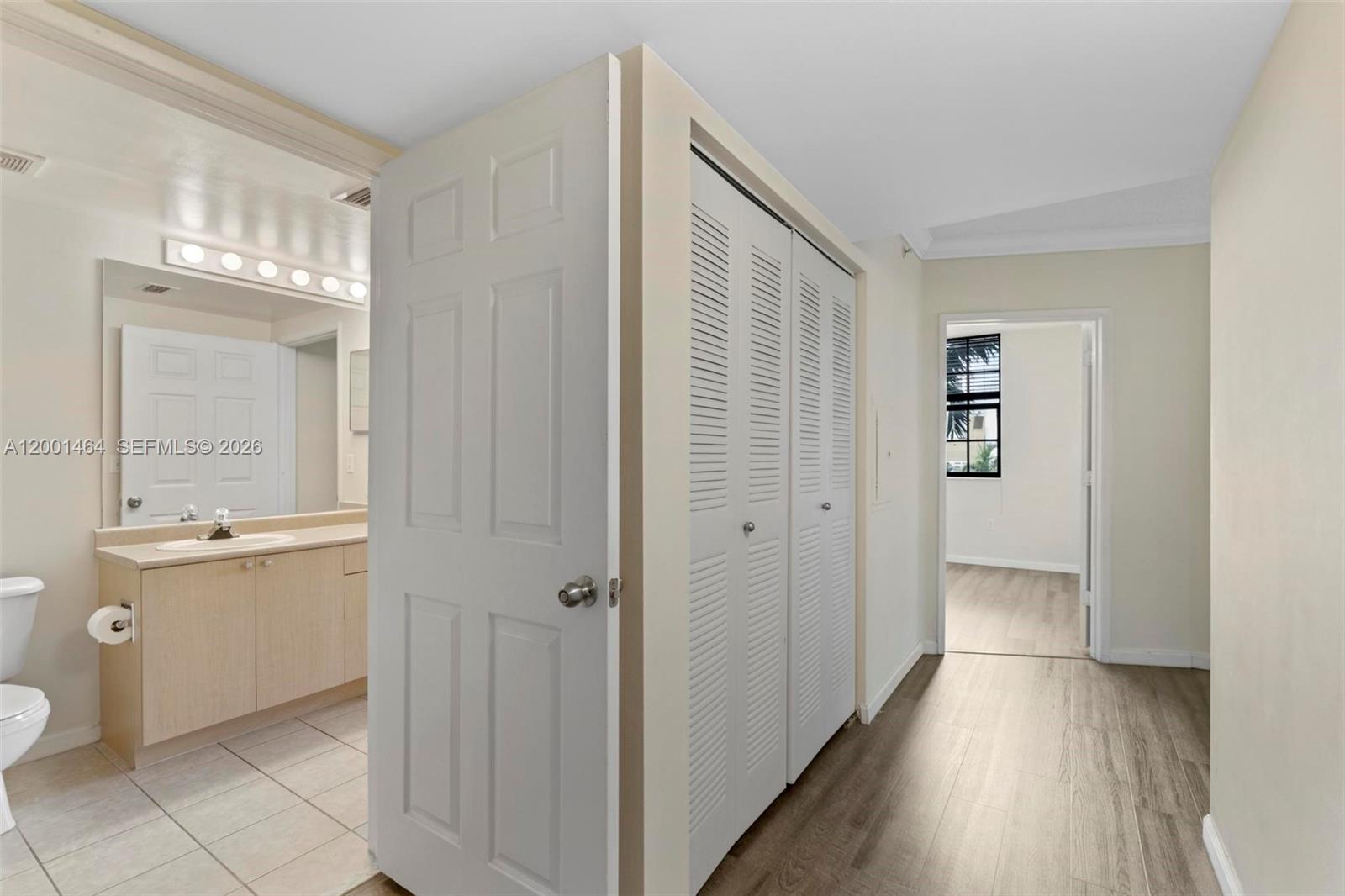 A bathroom with a vanity and a hallway featuring louvered closet doors and wood flooring — 1919 Van Buren St # 417A, Hollywood FL 33020, HOLLYWOOD, FL