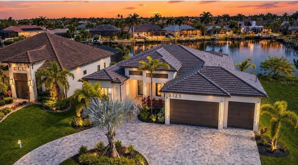 An aerial view of a modern house with a tiled roof, paver driveway, and waterfront backyard — 3123 SW 29TH AVENUE, CAPE CORAL, FL
