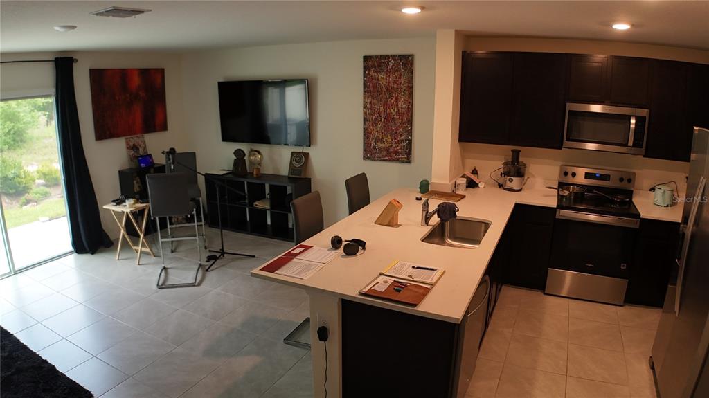 An open-concept kitchen and living area features dark cabinetry, stainless steel appliances, and tile flooring — 6569 SW 81ST LOOP, OCALA, FL