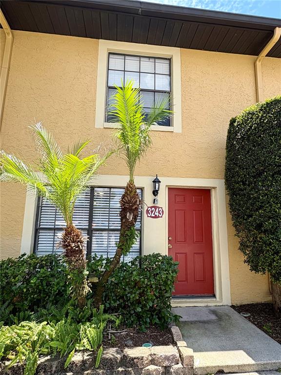 A two-story tan building features a red front door, a palm tree, and landscaping — 3243 FOREST OAKS COURT UNIT 117, WINTER PARK, FL