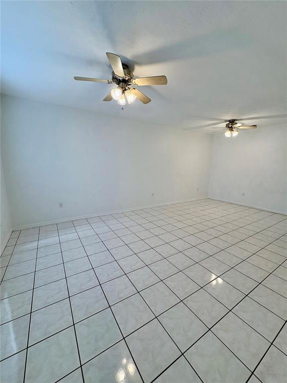 A spacious room features white tiled floors, plain white walls, and two ceiling fans — 3243 FOREST OAKS COURT UNIT 117, WINTER PARK, FL
