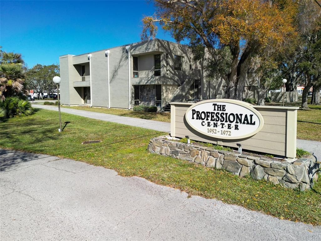 A two-story office building with light-colored siding stands behind a stone-based sign — 1964 BAYSHORE BOULEVARD UNIT B, DUNEDIN, FL