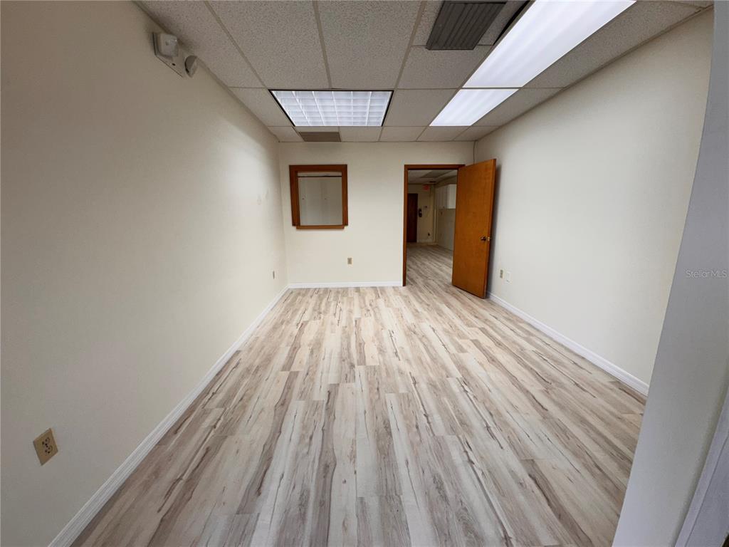 An empty office room features light wood-look flooring, white walls, and a drop ceiling — 1964 BAYSHORE BOULEVARD UNIT B, DUNEDIN, FL