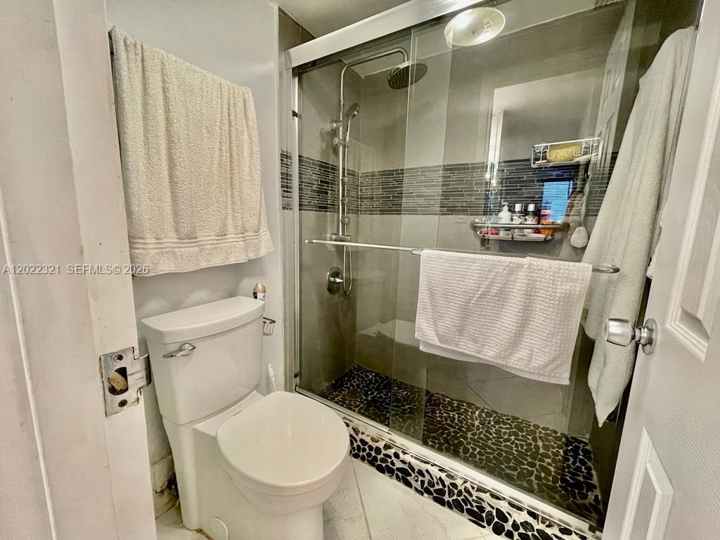 A bathroom features a white toilet, a glass-enclosed shower with pebble flooring, and gray tiling — 2030 S Ocean Dr # 801, Hallandale Beach FL 33009, HALLANDALE BEACH, FL
