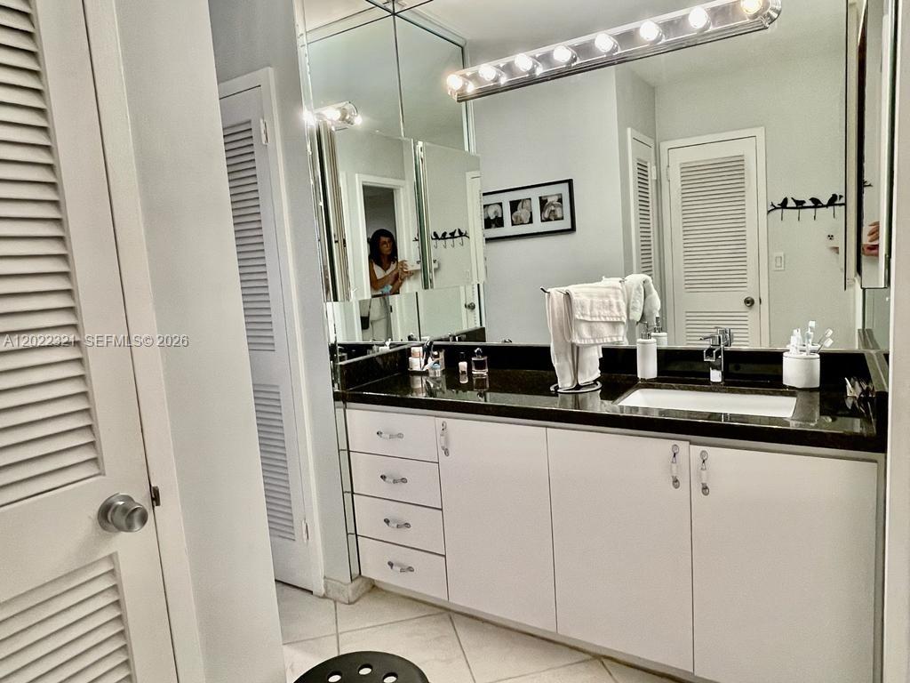 A bathroom features a dark countertop, white cabinets, a large mirror, and louvered closet doors — 2030 S Ocean Dr # 801, Hallandale Beach FL 33009, HALLANDALE BEACH, FL