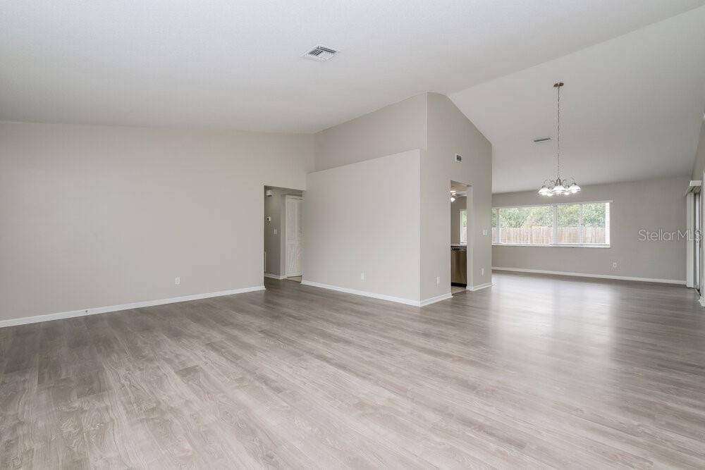 An open-concept living area with light gray walls, vaulted ceilings, and wood-look laminate flooring — 10142 BANNISTER STREET, SPRING HILL, FL