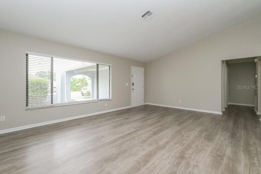 An empty living room with light gray walls, wood-look flooring, and a large window — 10142 BANNISTER STREET, SPRING HILL, FL
