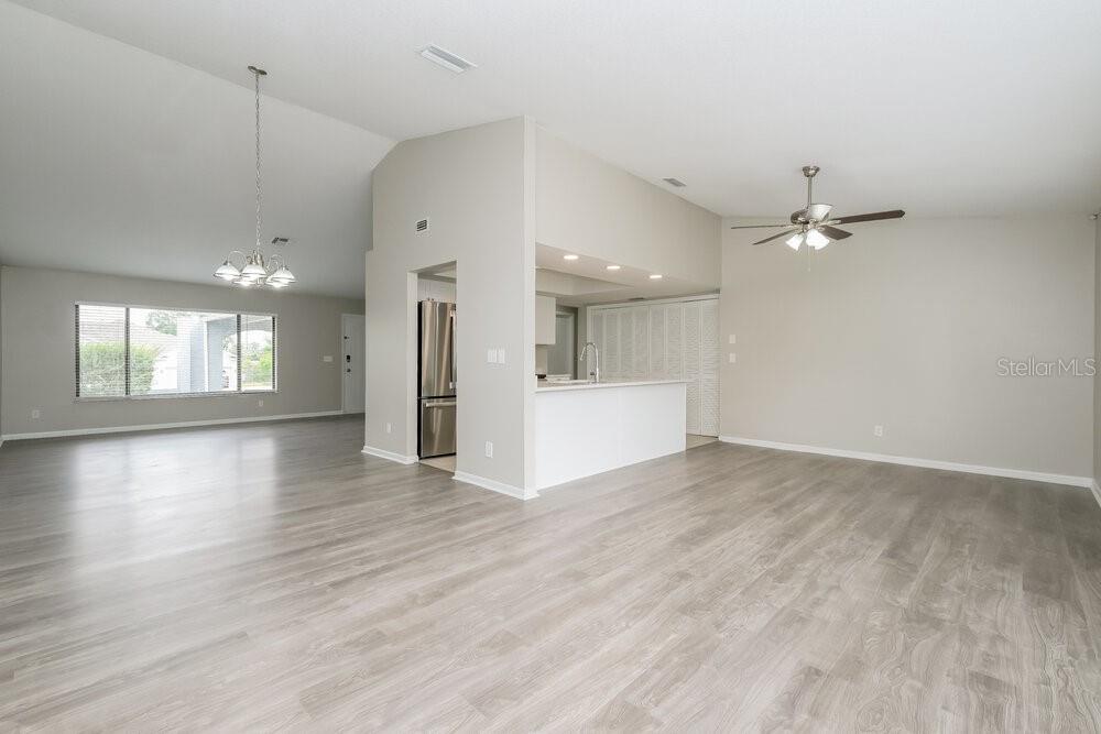A living room and kitchen area with light gray wood-look flooring and vaulted ceilings — 10142 BANNISTER STREET, SPRING HILL, FL
