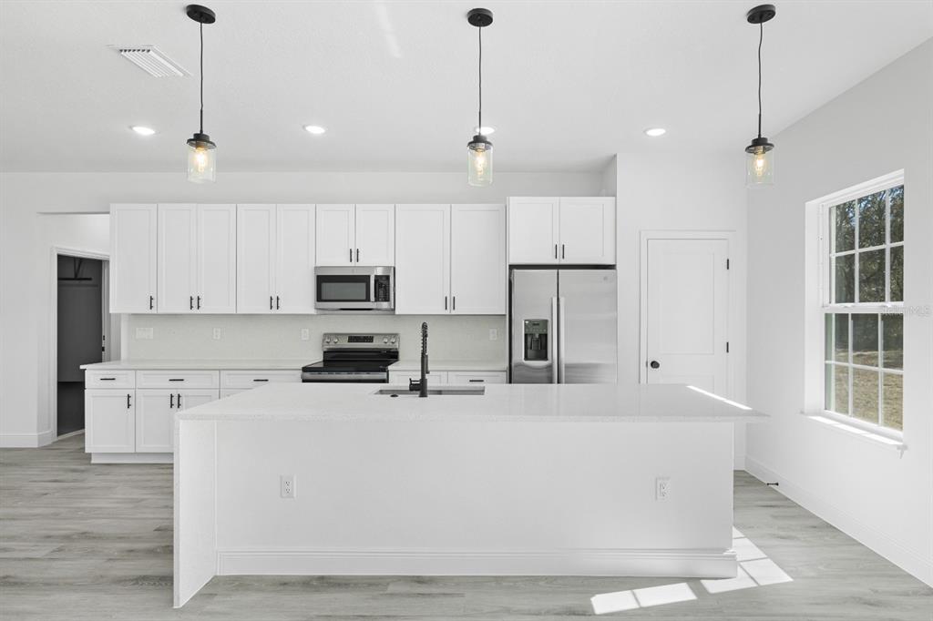 A modern kitchen features white cabinets, stainless steel appliances, a large island, and pendant lighting — 144 W RUSKA PLACE, CITRUS SPRINGS, FL