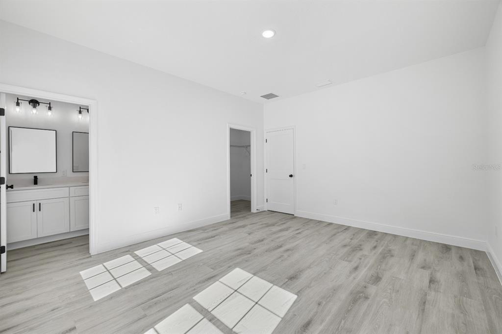 A bedroom with light gray wood-look flooring, white walls, an attached bathroom, and a closet — 144 W RUSKA PLACE, CITRUS SPRINGS, FL