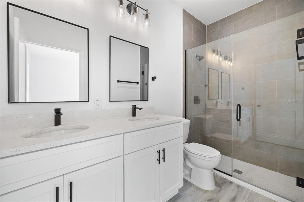 A modern bathroom features a double vanity with white cabinets, black fixtures, and a glass shower — 144 W RUSKA PLACE, CITRUS SPRINGS, FL