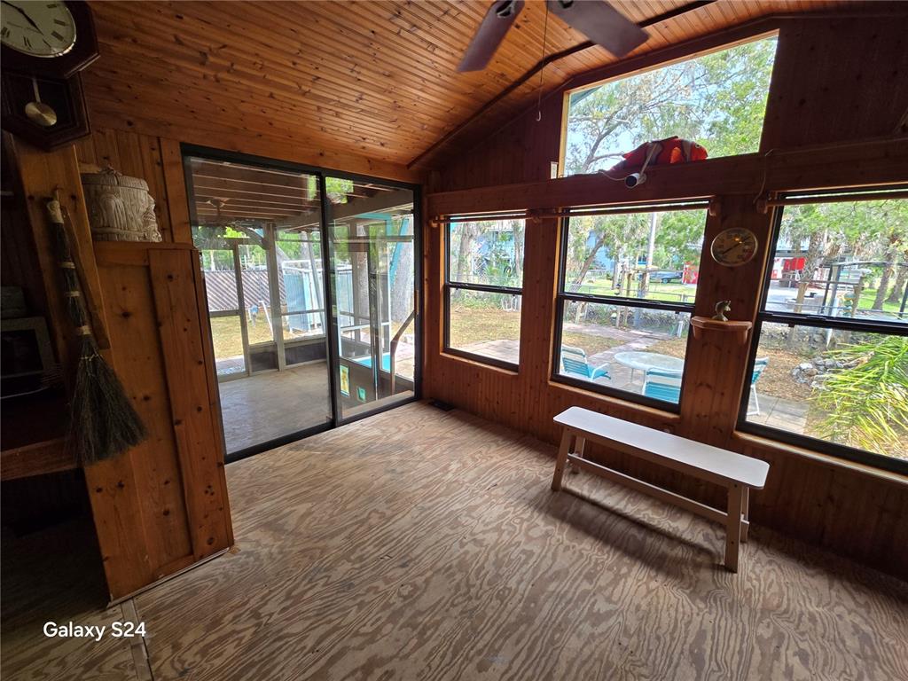 A sunroom with wood-paneled walls, a plywood floor, and large windows overlooking a yard — 14365 & 14353 W EBBTIDE COURT, CRYSTAL RIVER, FL