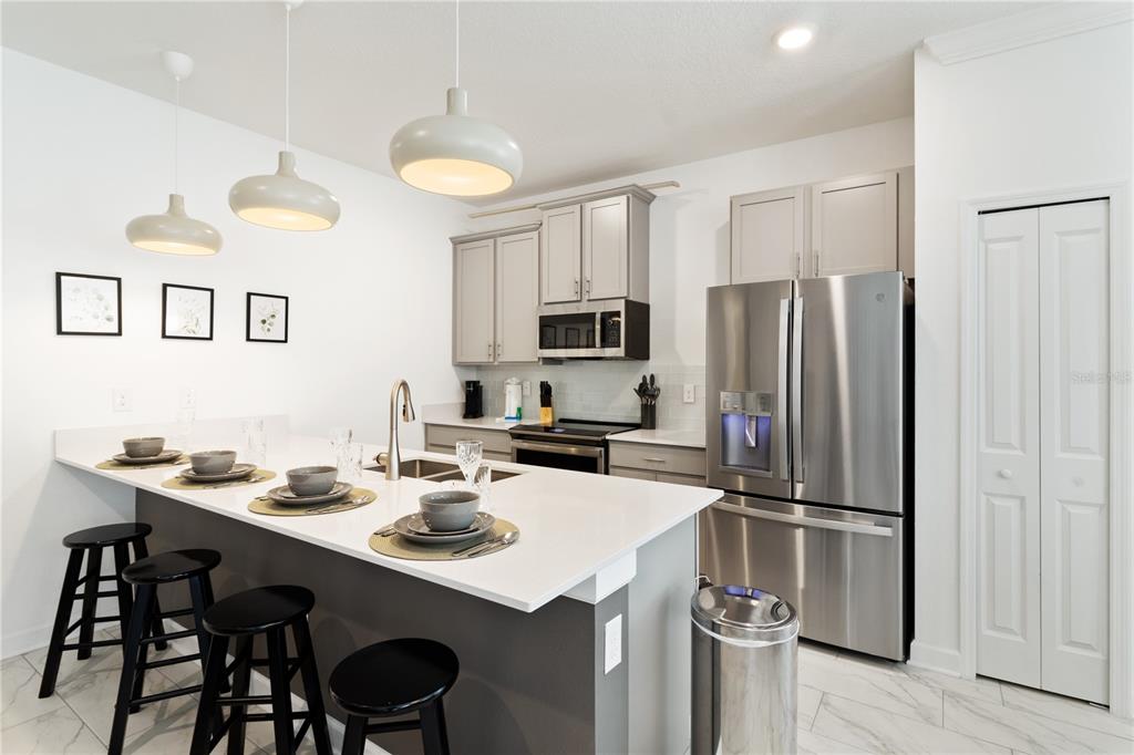 A modern kitchen features gray cabinets, stainless steel appliances, and a white quartz island countertop — 4184 PARAGRAPH DRIVE, KISSIMMEE, FL