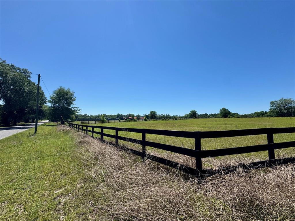 A black wooden fence borders a large, grassy field under a clear blue sky — 0 NW 115 AVENUE, OCALA, FL
