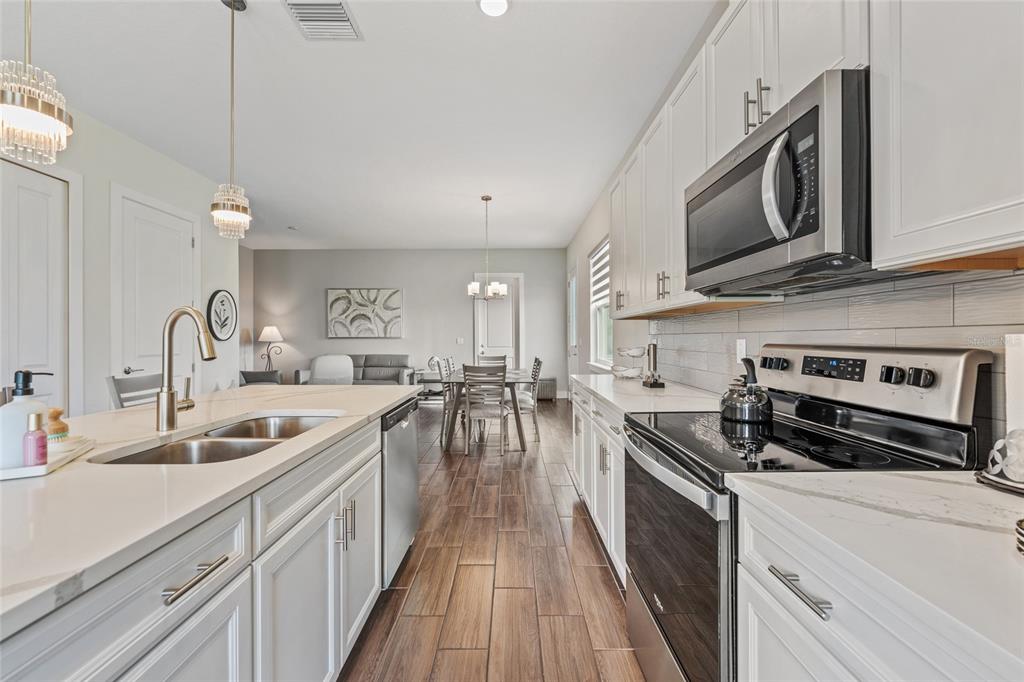 A modern kitchen with white cabinets, stainless steel appliances, and wood-look tile flooring — 1470 BROOKDALE COURT, OVIEDO, FL