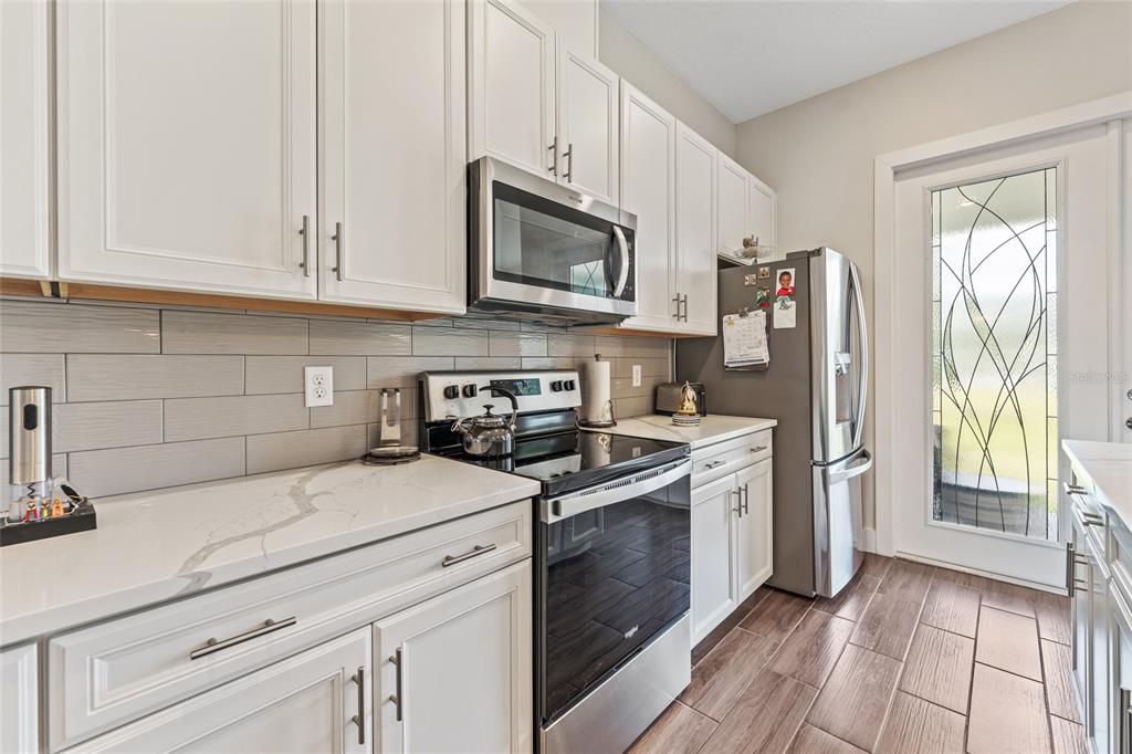A kitchen features white cabinets, stainless steel appliances, gray subway tile backsplash, and wood-look flooring — 1470 BROOKDALE COURT, OVIEDO, FL