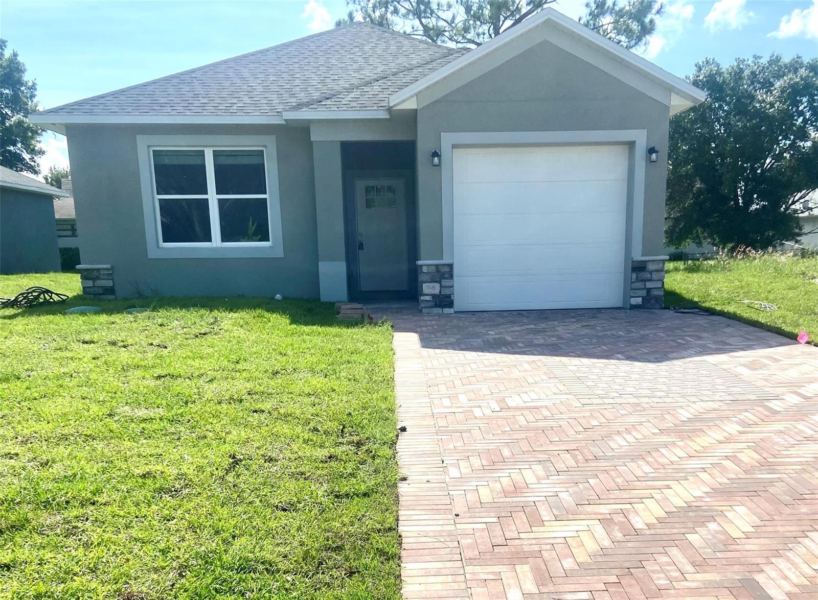A single-story house with a gray stucco exterior, a white garage door, and a brick driveway — 4229 Elson Avenue, Sebring FL 33875, SEBRING, FL
