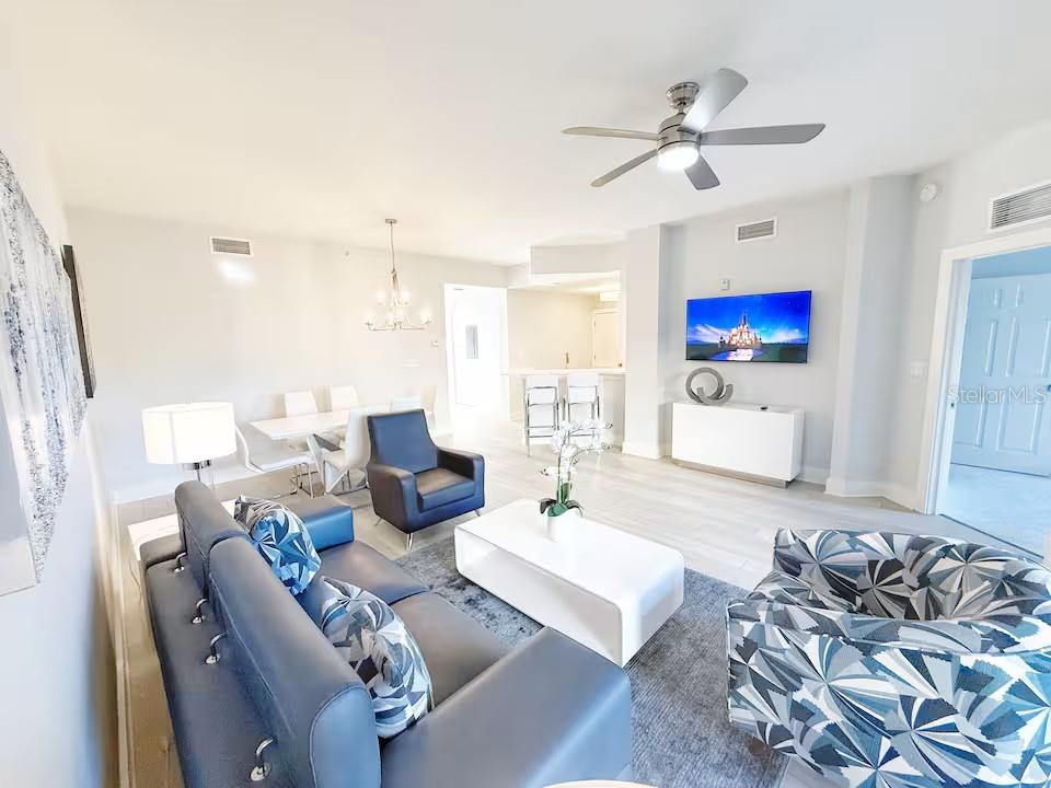 A modern living room features a blue sofa, patterned armchair, white coffee table, and television — 8762 WORLDQUEST BOULEVARD UNIT 6204, ORLANDO, FL