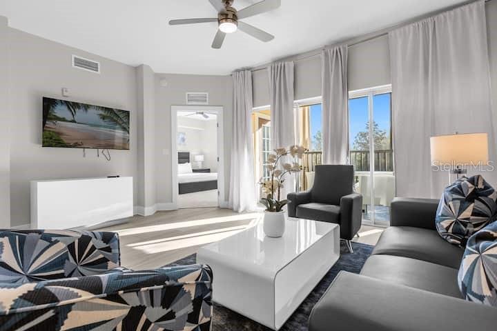 A modern living room features a gray sofa, patterned armchairs, a white coffee table, and balcony access — 8762 WORLDQUEST BOULEVARD UNIT 6204, ORLANDO, FL