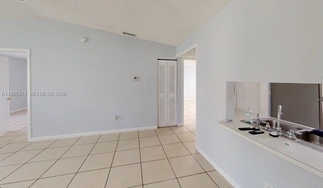 A room with light-colored tile flooring, pale blue walls, and a kitchen pass-through window — 9481 W Fern Ln, Miramar FL 33025, MIRAMAR, FL