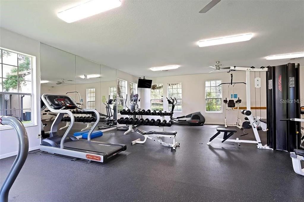 A gym room features a treadmill, weight rack, multi-station machine, and wall-to-wall mirrors — 6292 TWAIN STREET UNIT 102, ORLANDO, FL