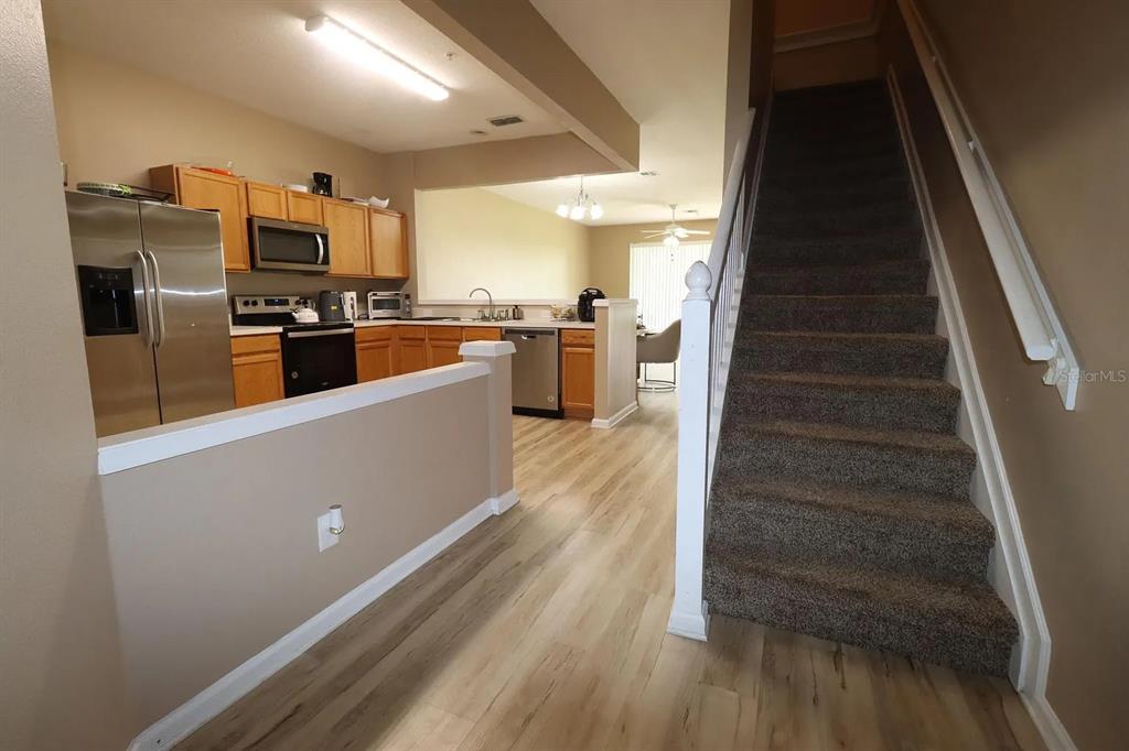 A kitchen with wood cabinets and stainless appliances sits beside a carpeted staircase — 6292 TWAIN STREET UNIT 102, ORLANDO, FL