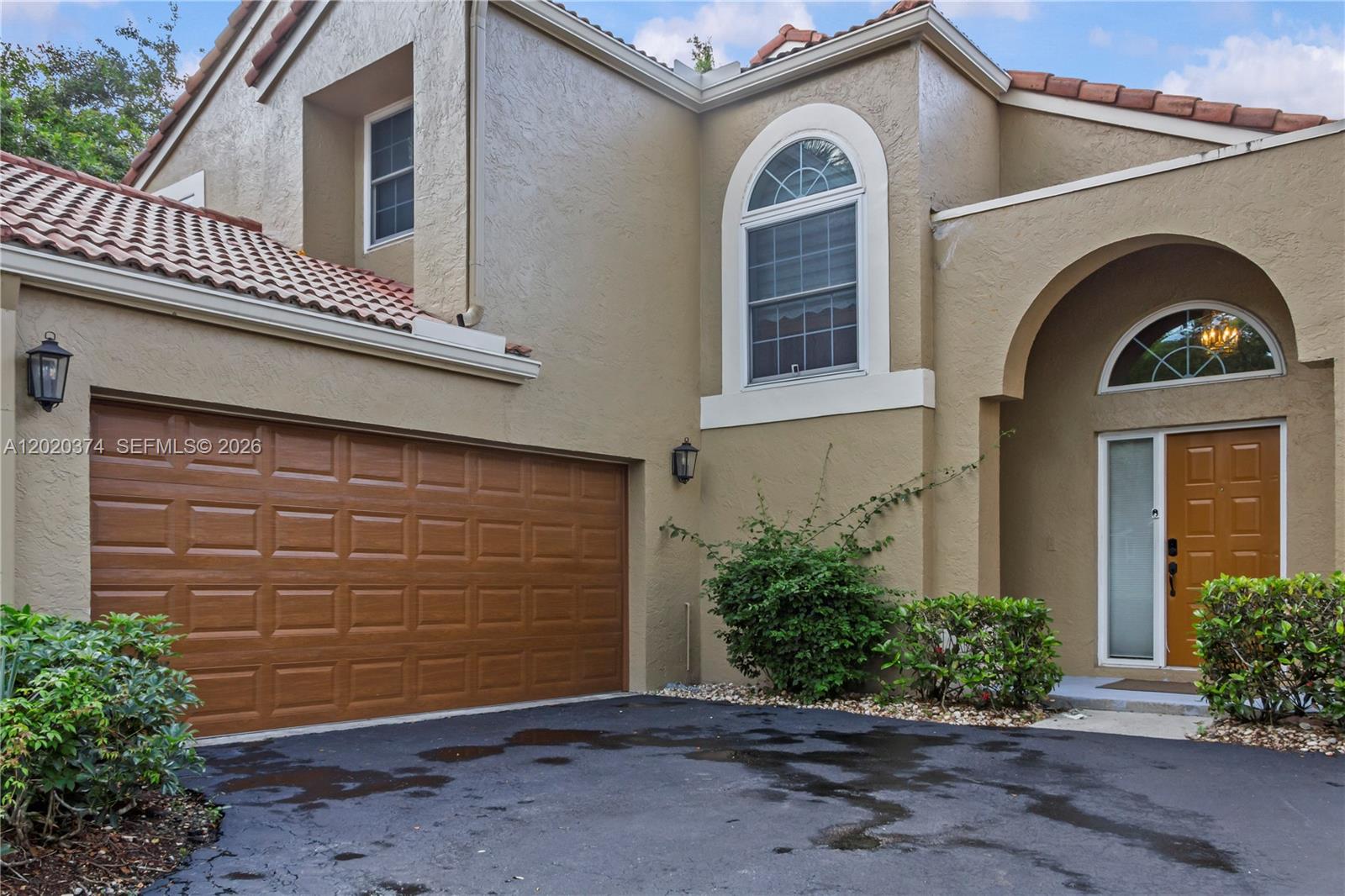 The exterior of a two-story stucco home features a garage, arched entryway, and tiled roof — 6885 NW 75th Pl, Parkland FL 33067, PARKLAND, FL