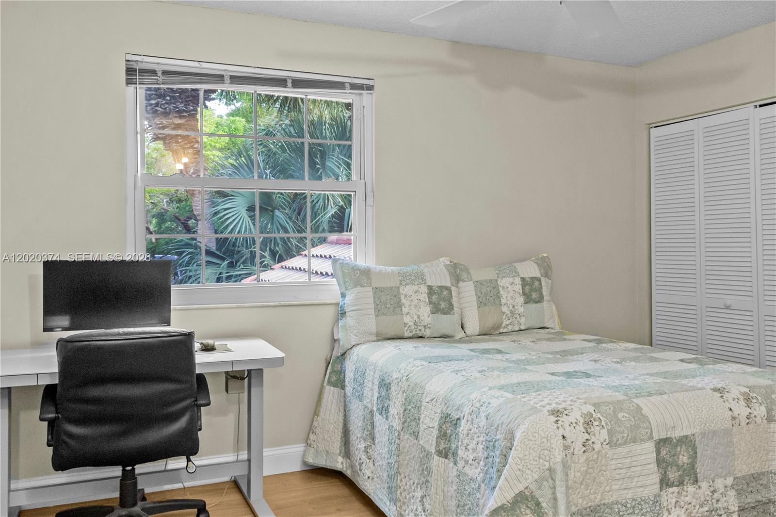 A bedroom features a bed with a patchwork quilt, a desk, and a window view — 6885 NW 75th Pl, Parkland FL 33067, PARKLAND, FL