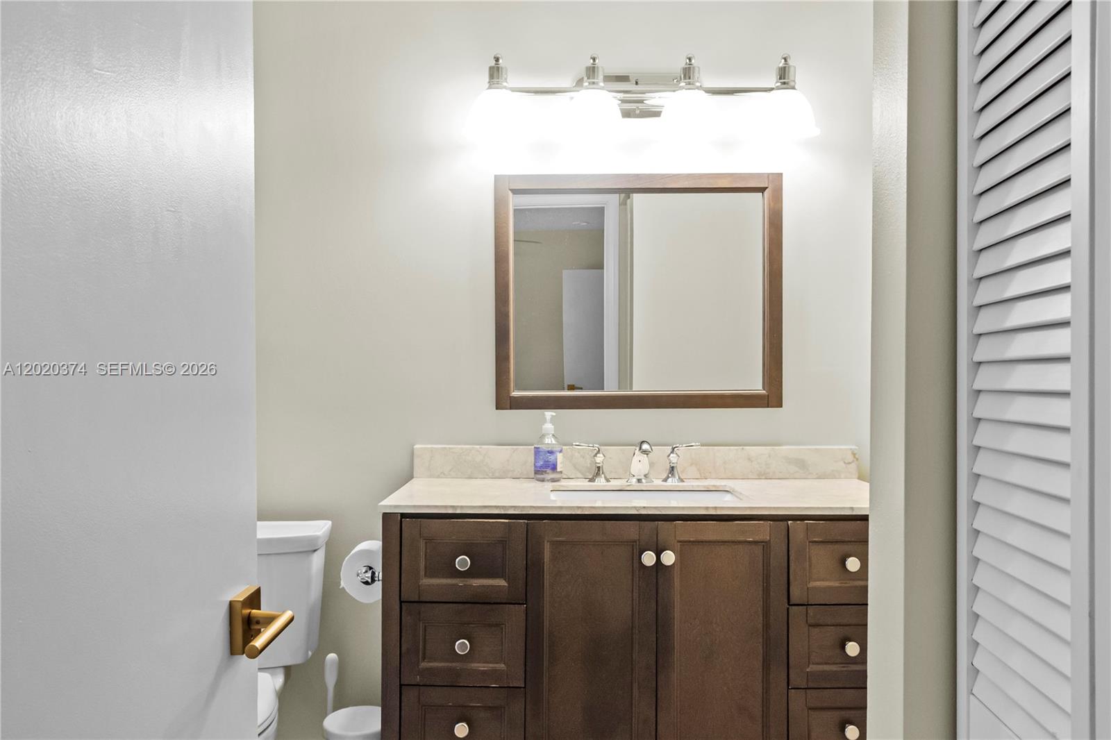 A bathroom features a dark wood vanity, a marble countertop, and a wall-mounted mirror — 6885 NW 75th Pl, Parkland FL 33067, PARKLAND, FL