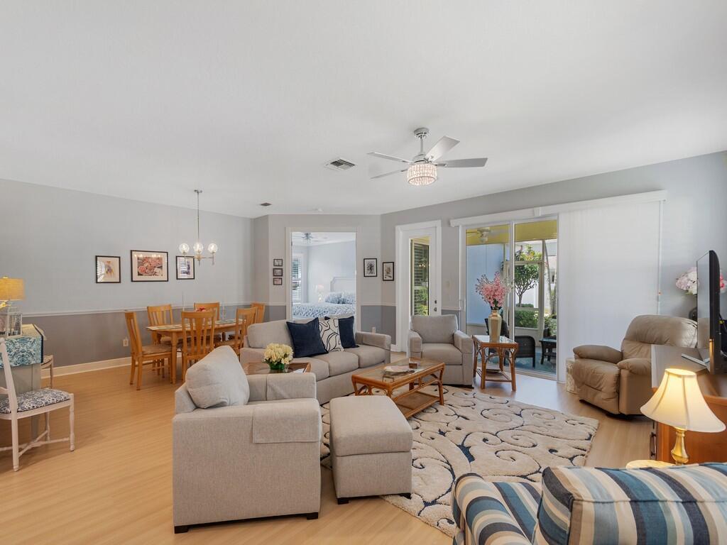 An open-concept living and dining area features light wood flooring, neutral walls, and sliding doors — 7780 14th Lane, Vero Beach FL 32966, VERO BEACH, FL