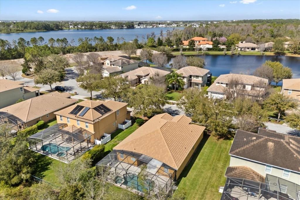 An aerial view shows several suburban houses with swimming pools and screened lanais near a lake — 9122 STROMBOLI COURT, KISSIMMEE, FL